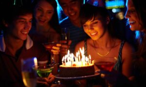Teen girl on her birthday looking at birthday cake surrounded by friends