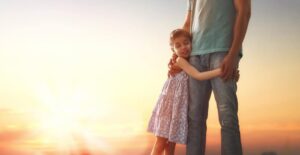 Young girl clinging to her father with sunset in the background