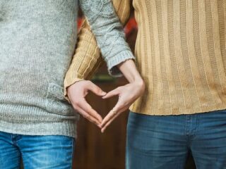 Man and woman standing side by side making a heart sign with their hands
