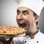 Goofy picture of a man in a chef's hat pretending to bite into a whole pizza