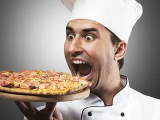Goofy picture of a man in a chef's hat pretending to bite into a whole pizza