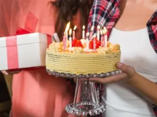 Close up of people carrying a birthday cake and present for a birthday party