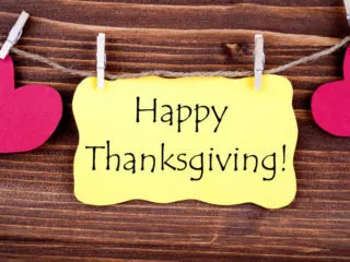 Yellow note with the words Happy Thanksgiving written on it, pinned in front of a wood background