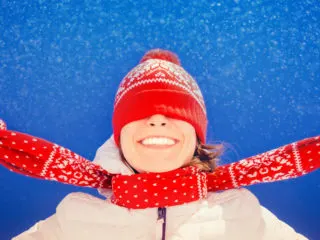 Closeup of a silly young woman with a scarf over her eyes looking up at falling snowflakes