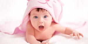 Baby with funny expression peeking out from under blanket