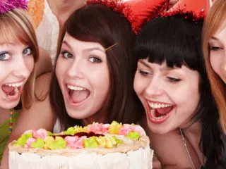 Group of smiling young women crowded around a cake at an 18th birthday party