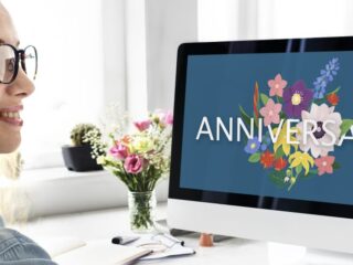 Woman sitting at her work desk looking a a computer with the word Anniversary on the screen