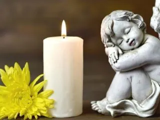 Angel statue near flower and candle, symbolizing memorial to deceased loved one