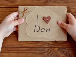 Child's hands holding a homemade card that says I love dad on the outside